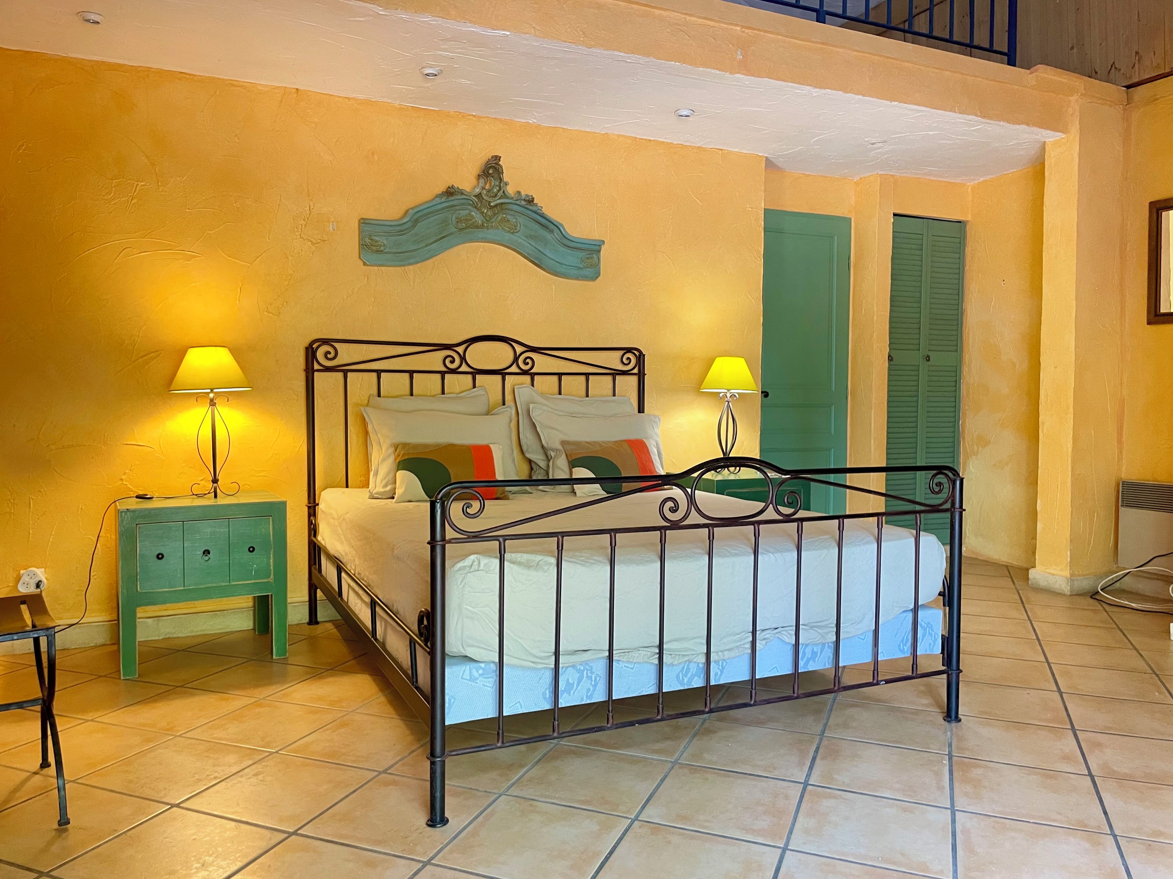A bedroom with a bed, two nightstands, a wall-mounted lamp, and a green door.