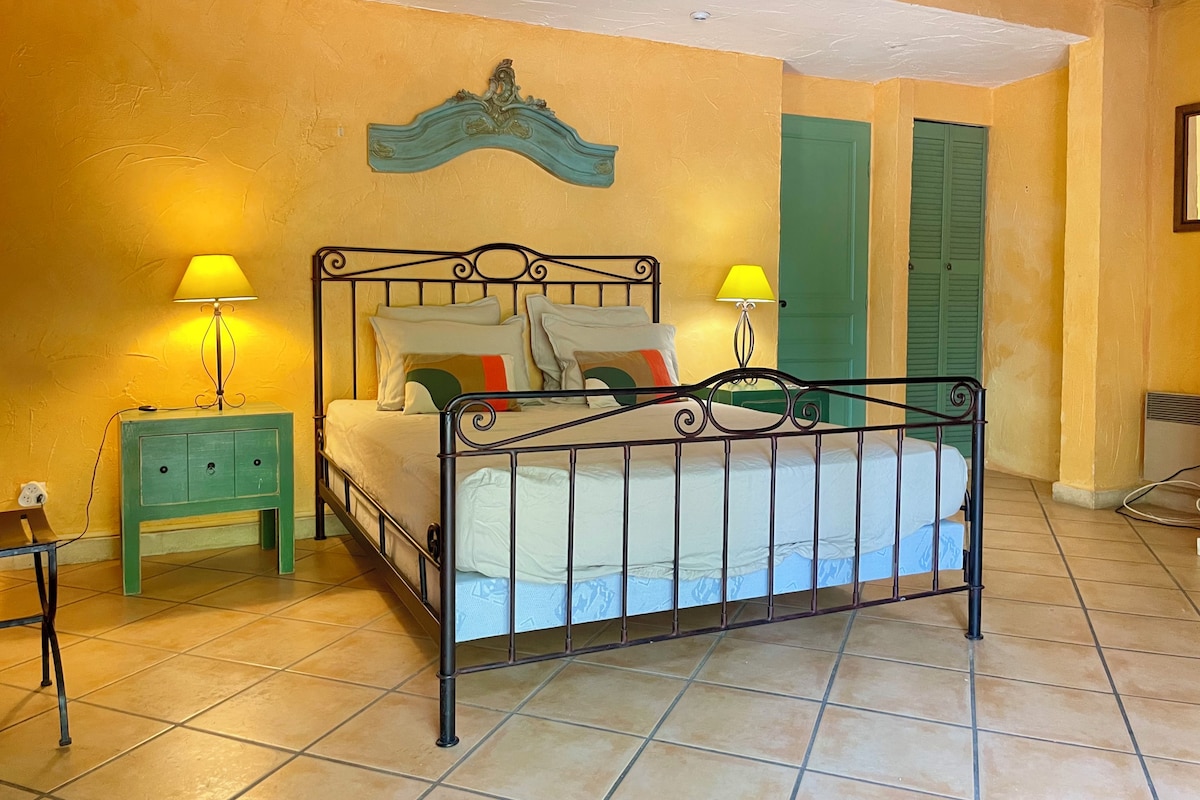 A bedroom with a bed, two nightstands, a wall-mounted lamp, and a green door.