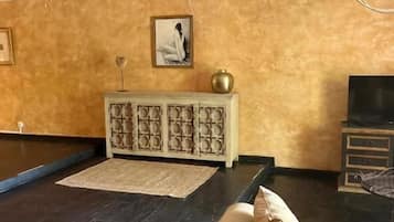 A room with a dark wooden floor, a beige sofa, a white cabinet, a ceiling fan, and a television.