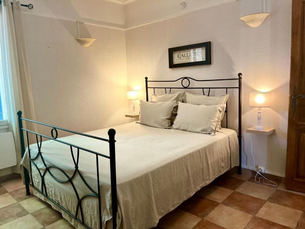 A neatly made bed with a metal frame and white bedding, a wall-mounted lamp, and a framed sign above the bed.