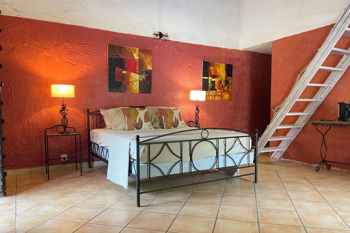 A bedroom with a bed, two bedside lamps, a ladder, and two abstract paintings on the walls.