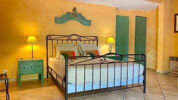 Un dormitorio con estructura de cama metálica, dos mesitas de noche con lámparas, una puerta verde y un adorno decorativo sobre la cama.