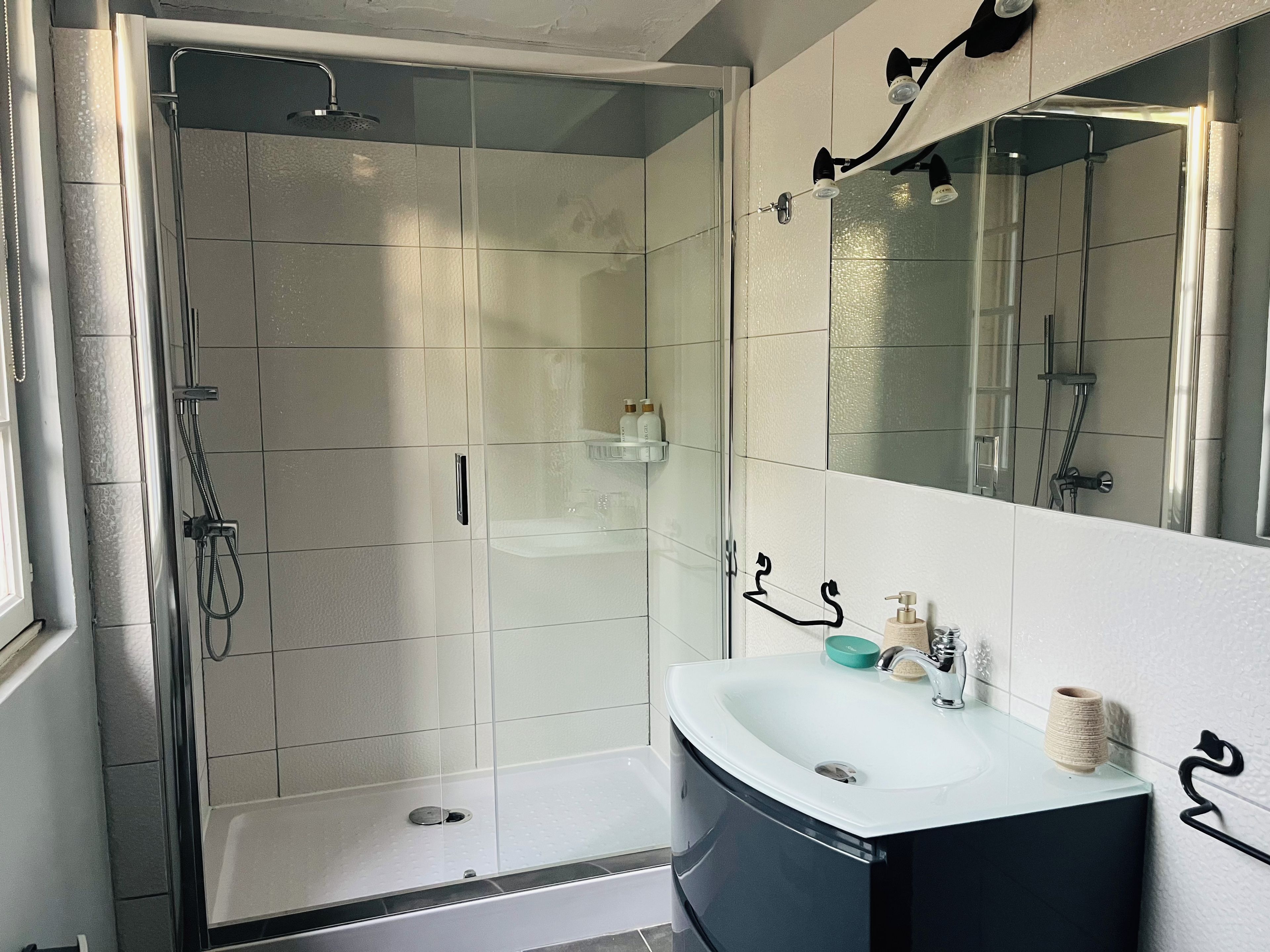 Un baño moderno con ducha envuelta en vidrio, un lavabo blanco con gabinete negro y un espejo grande.