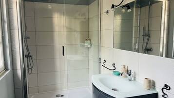 Un baño moderno con ducha envuelta en vidrio, un lavabo blanco con gabinete negro y un espejo grande.