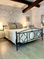 Une chambre avec un lit en métal, un plancher en bois et un mur en pierre.