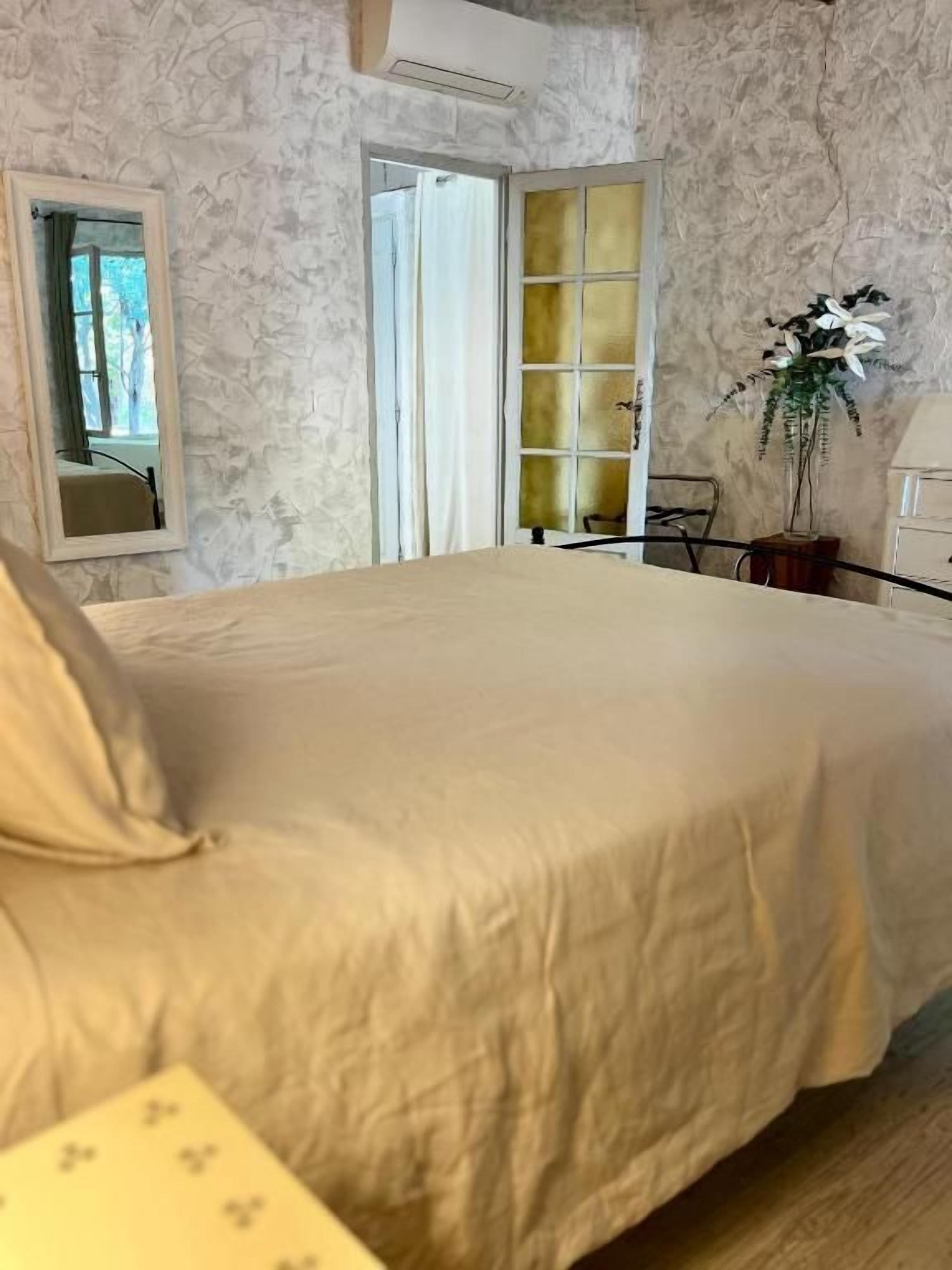 Een slaapkamer met een groot bed, een spiegel, een raam en een deur naar een andere kamer.