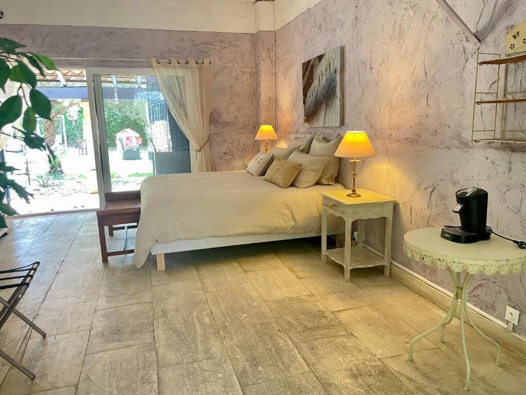 A bedroom with a bed, bedside lamps, a coffee machine, and a view through a glass door.