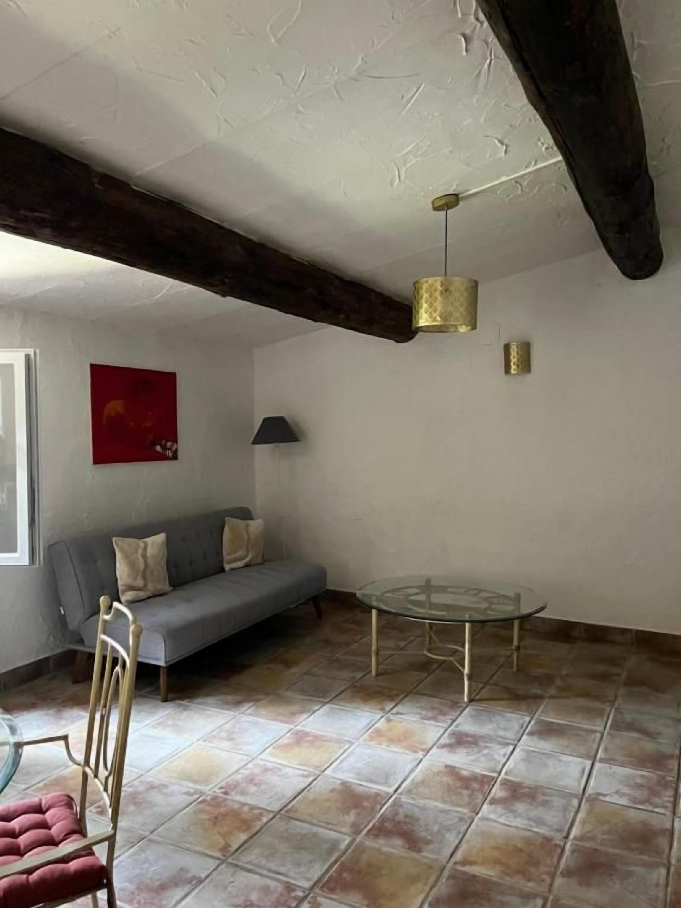 Una habitación con un sofá gris, una mesa de vidrio y una silla.