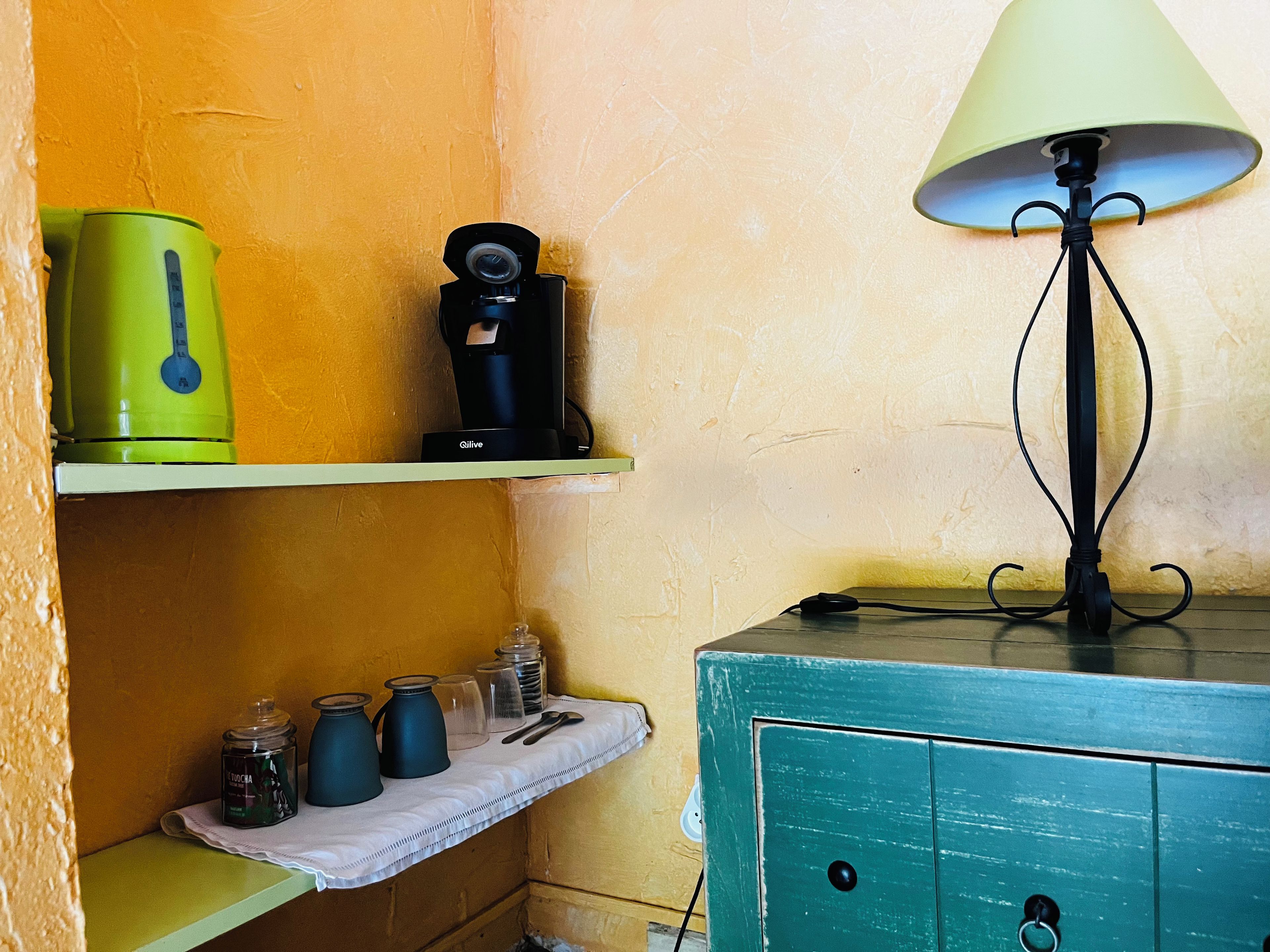 A kitchen area with a green kettle, a coffee maker, and jars on a shelf.