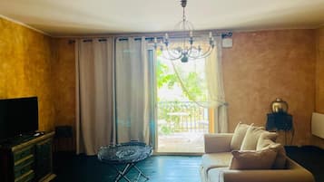 A living room with a sofa, a television, a chandelier, and a view of the outdoors through a window.