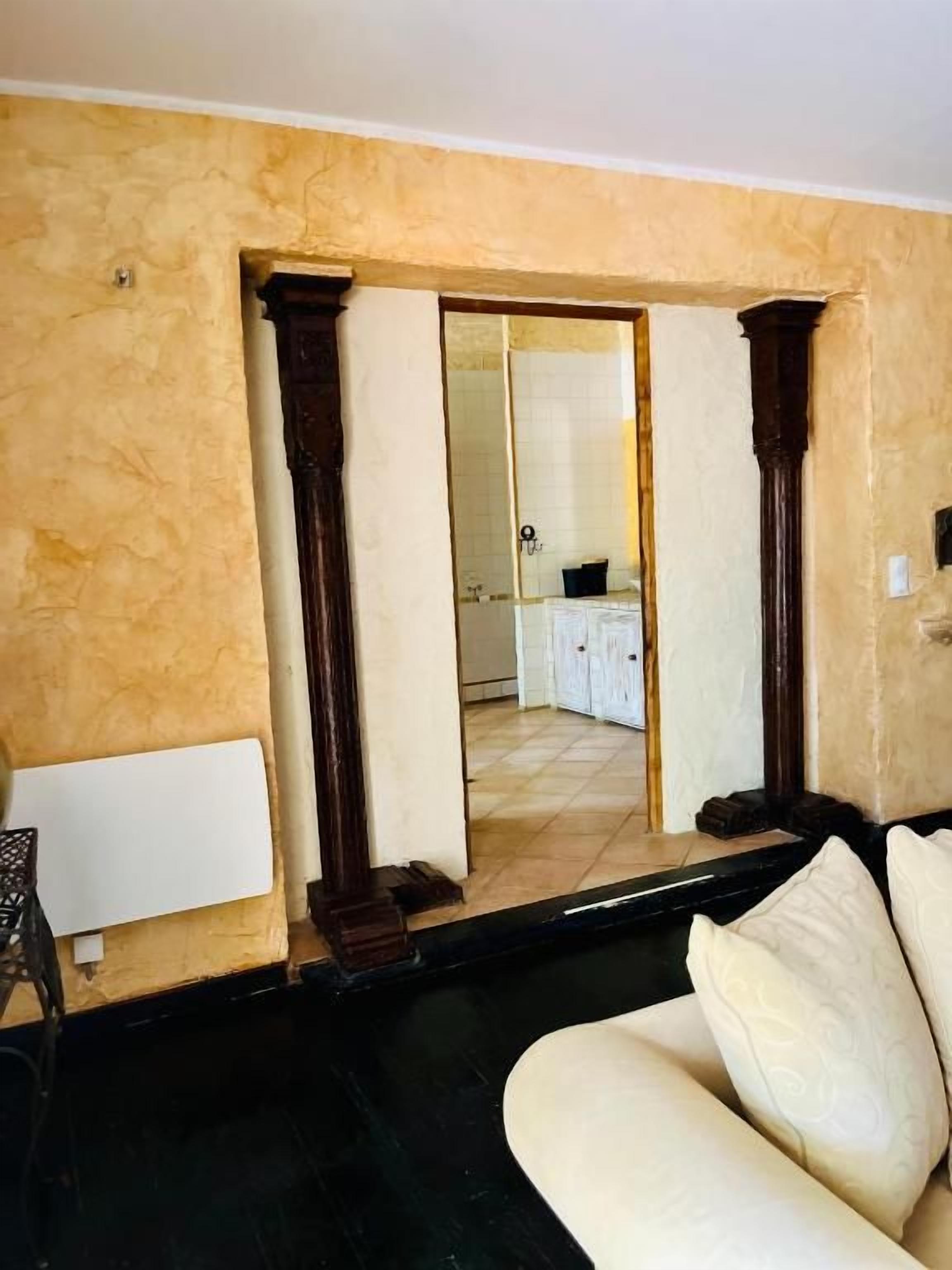 A room with a beige textured wall, a dark wooden floor, a white sofa, and a doorway leading to a kitchen area.