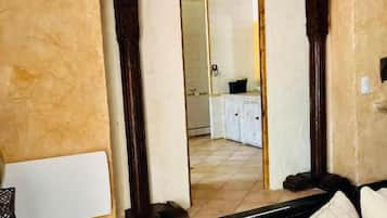 A room with a beige textured wall, a dark wooden floor, a white sofa, and a doorway leading to a kitchen area.