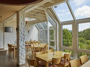 A dining area with wooden tables and chairs, large windows, and a stone wall. - 2 Person Holiday Park Home in Willingen (Willingen)