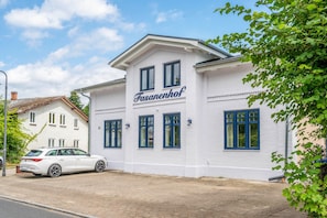Ein weißes Gebäude mit der Aufschrift 'Fasanenhof' an der Fassade, mit zahlreichen Fenstern und einem gepflasterten Eingangsbereich.
