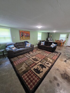 A living room with two couches, a rug with animal prints, a painting on the wall, and a dining area in the background. - Cabin with spacious yard north of Dover Ar.  National Forest, Moccasin Gap ATV (Dover)