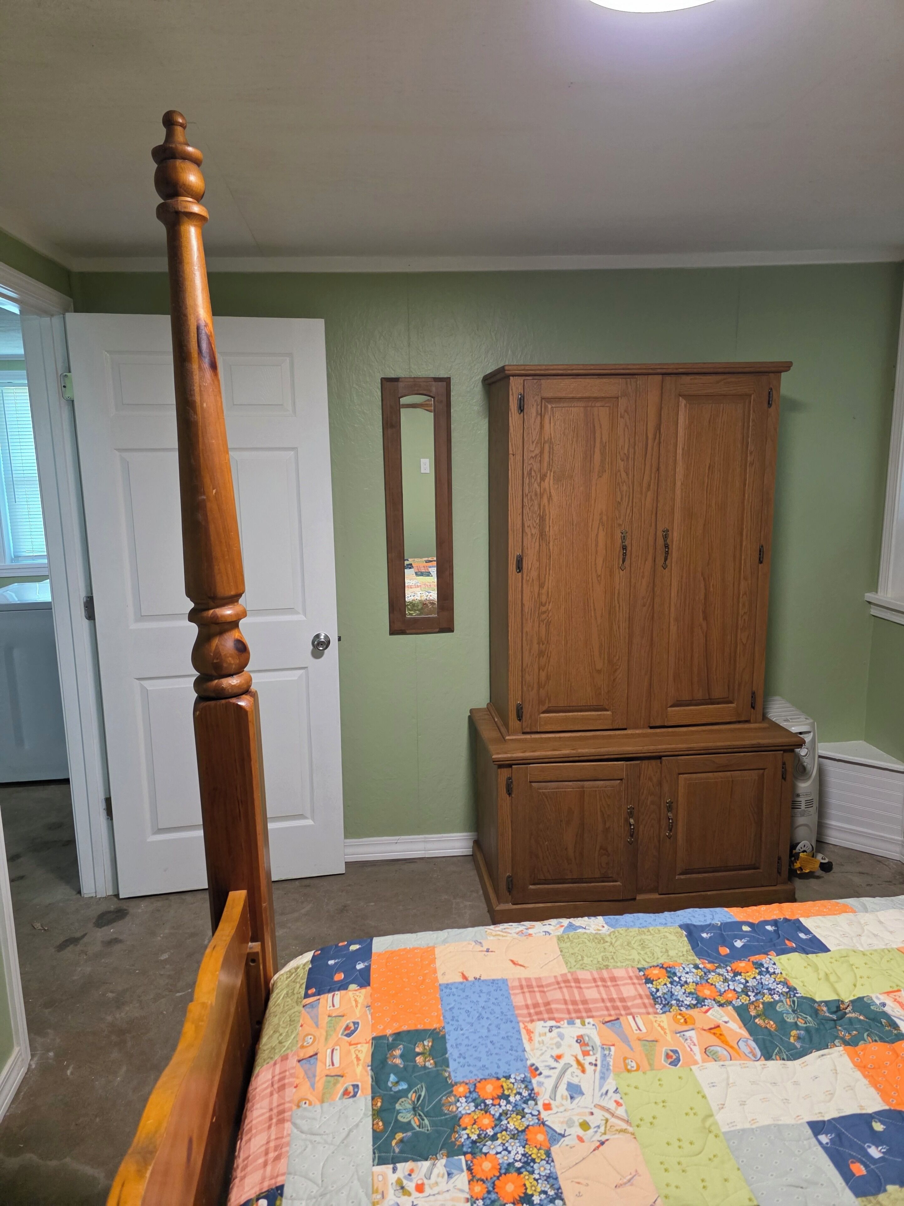 Een slaapkamer met een houten baldakijn, een houten garderobe en een sprei op het bed.