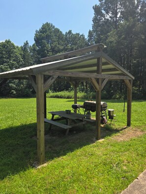 A wooden picnic shelter with a table and grill in a grassy field. - Cabin with spacious yard north of Dover Ar.  National Forest, Moccasin Gap ATV (Dover)