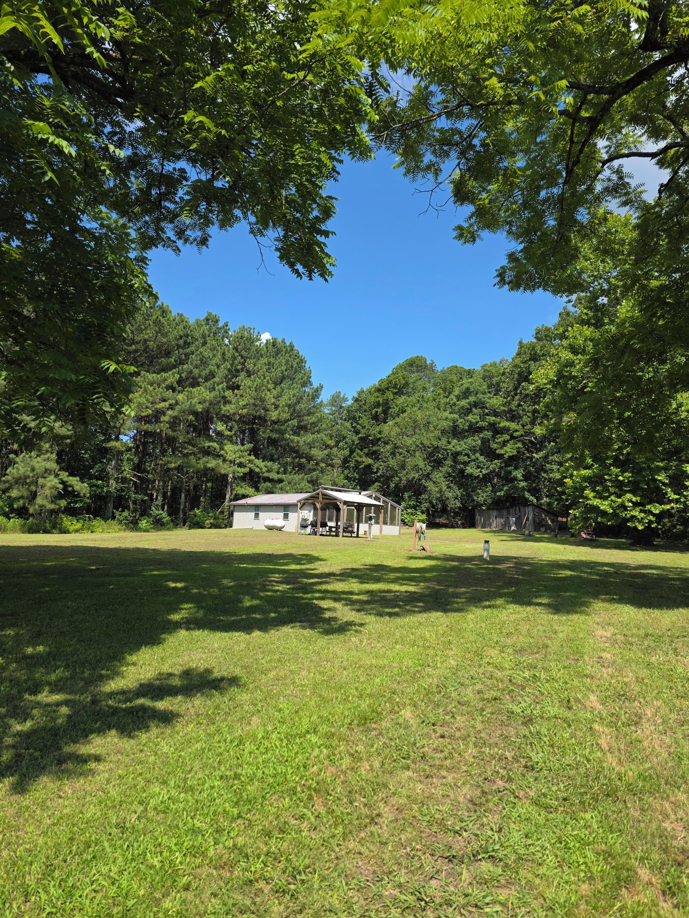 A grassy field with a wooden structure, possibly a gazebo, and a building in the background.