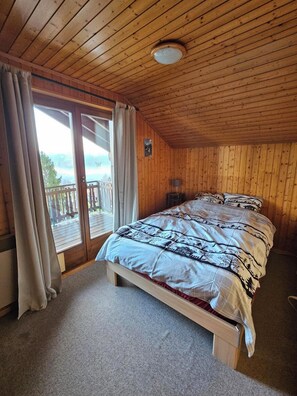 Ein Zimmer mit Holzwandverkleidung, einem Bett, einem kleinen Tisch und Blick durch eine Glastür.