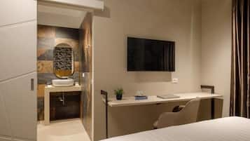 A modern hotel room with a bed, a desk, a flat-screen TV, and a bathroom with a vanity and mirror.