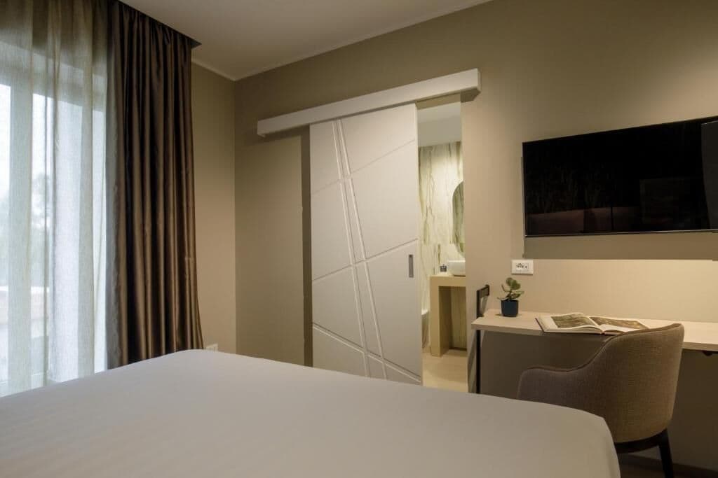 Habitación de hotel con cama, escritorio, silla, televisión y puerta corrediza que da al baño.