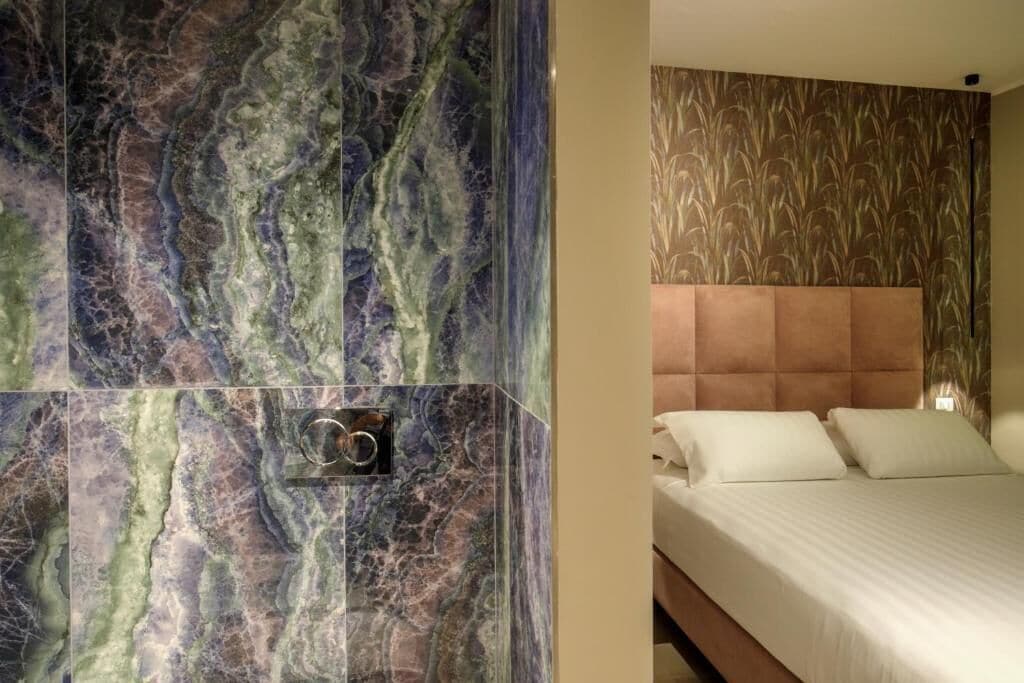 A hotel room with a bed, a headboard, and a wall with a marble-like pattern.