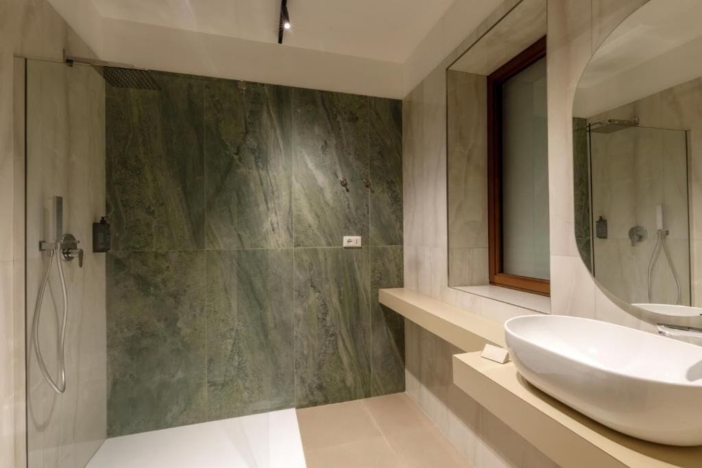 A modern bathroom with a large mirror, a freestanding bathtub, and a marble wall.