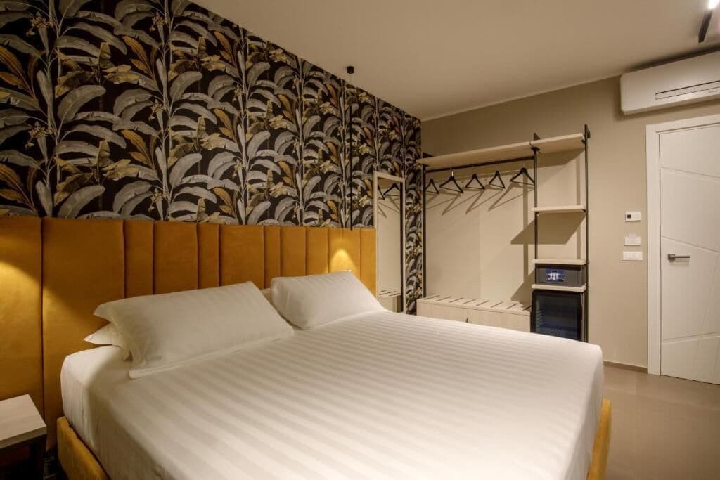 Quarto de hotel com cama, guarda-roupa, espelho e parede com padrão de folhas.