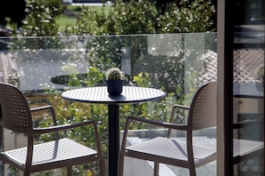 A round table with a potted cactus, two metal chairs, and a glass balustrade overlooking a garden.