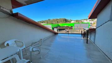 Uma varanda com cadeiras de plástico branco, chão de azulejos e vista para um estacionamento com estrutura verde.