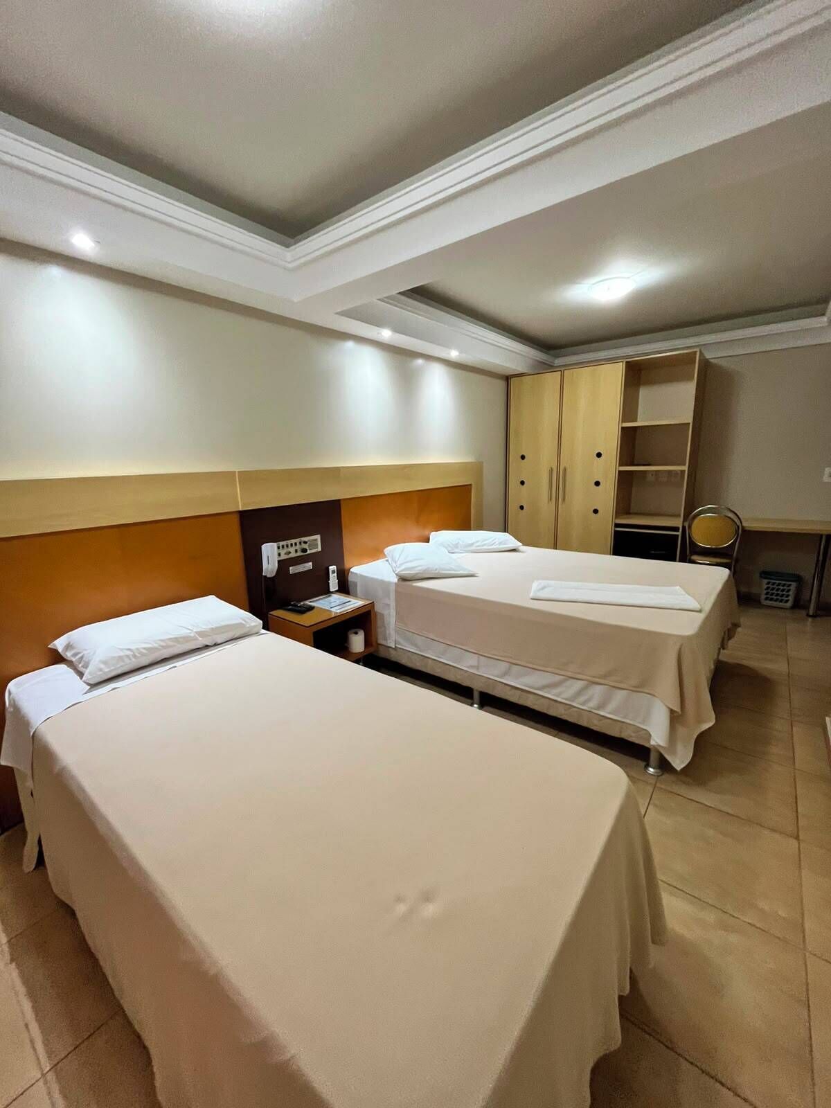 A hotel room with two beds, a wardrobe, a desk, and a small kitchenette.