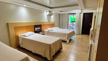 A hotel room with three beds, a headboard, a ceiling light, and a door leading to a balcony.