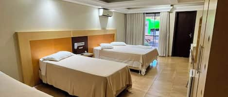 Habitación de hotel con tres camas, cabecera, una lámpara en el techo y una puerta que da a un balcón.