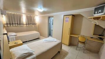 A compact hotel room with a single bed, a desk, a chair, a wardrobe, and a television.