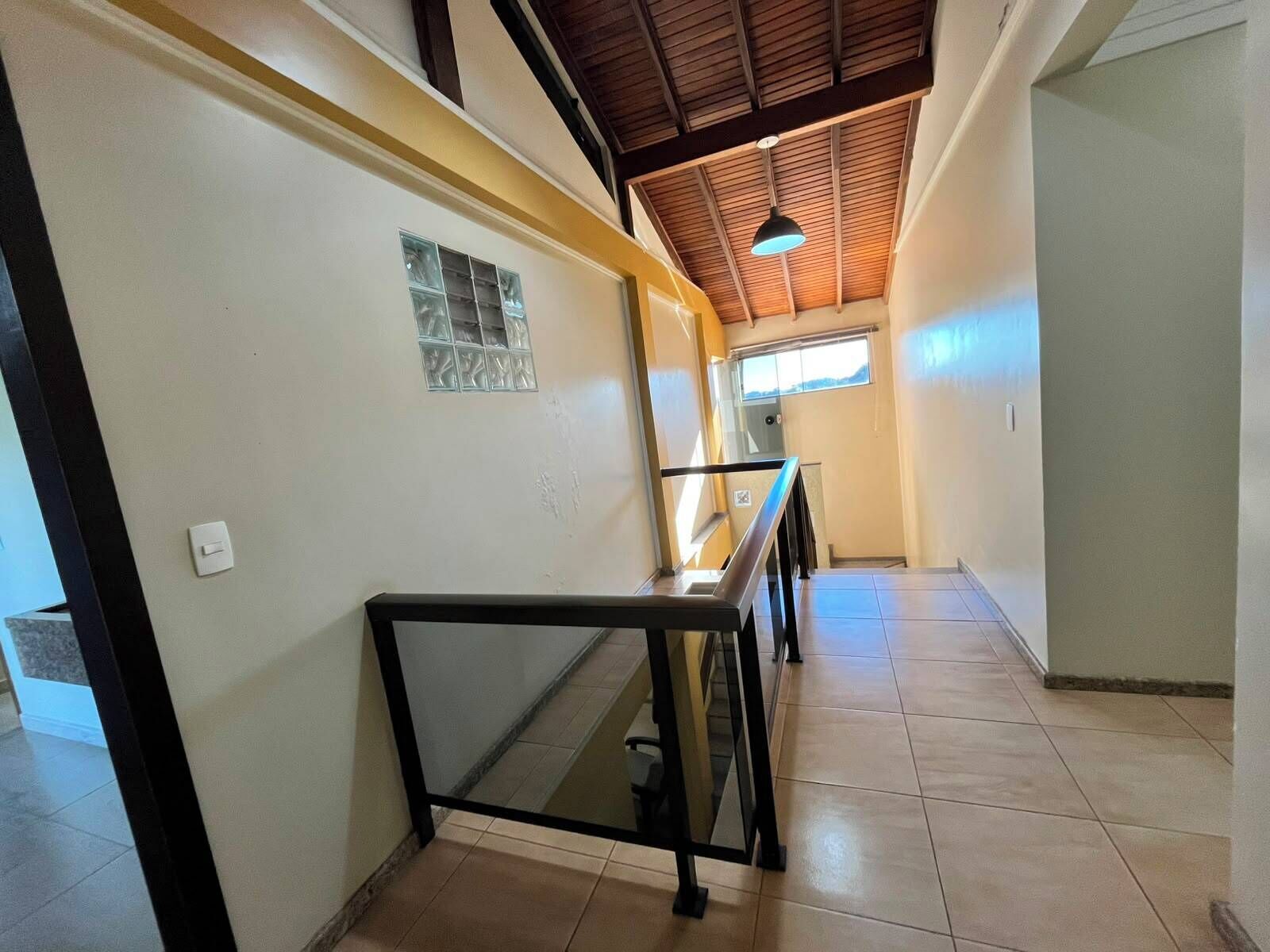 Un corridoio con pavimento piastrellato, ringhiera in vetro e soffitto a travi in legno.