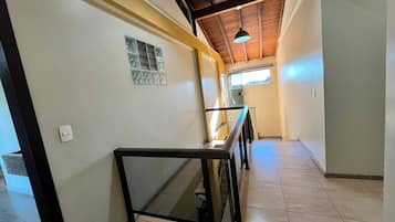 A hallway with a tiled floor, a glass railing, and a ceiling with wooden beams.