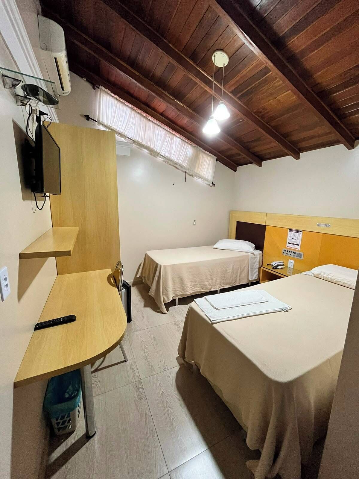 A hotel room with two single beds, a desk with a chair, a TV, and a window with curtains.