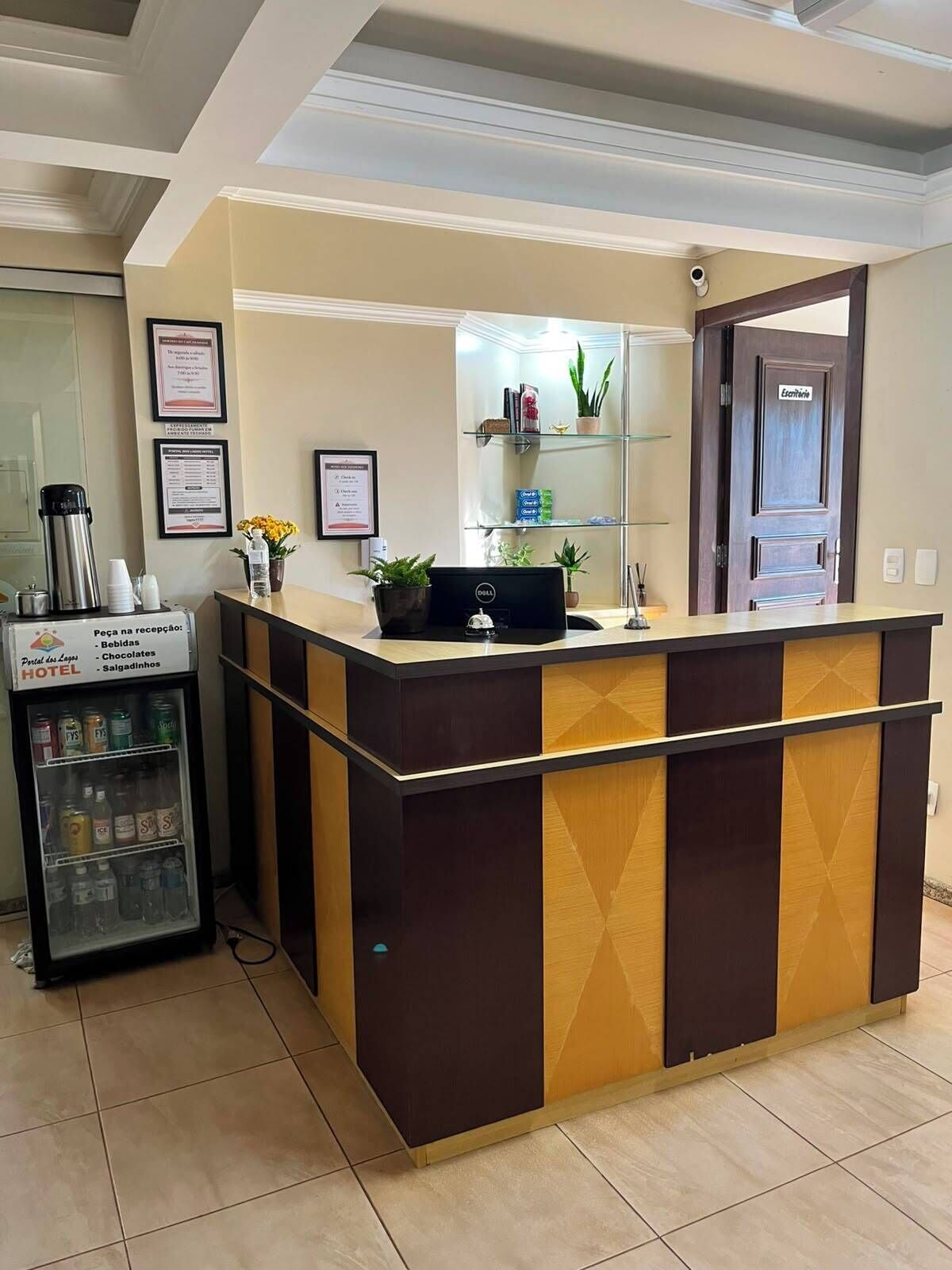 A hotel reception area with a reception desk, a refrigerator stocked with beverages, and a door labeled 'Estácio.'