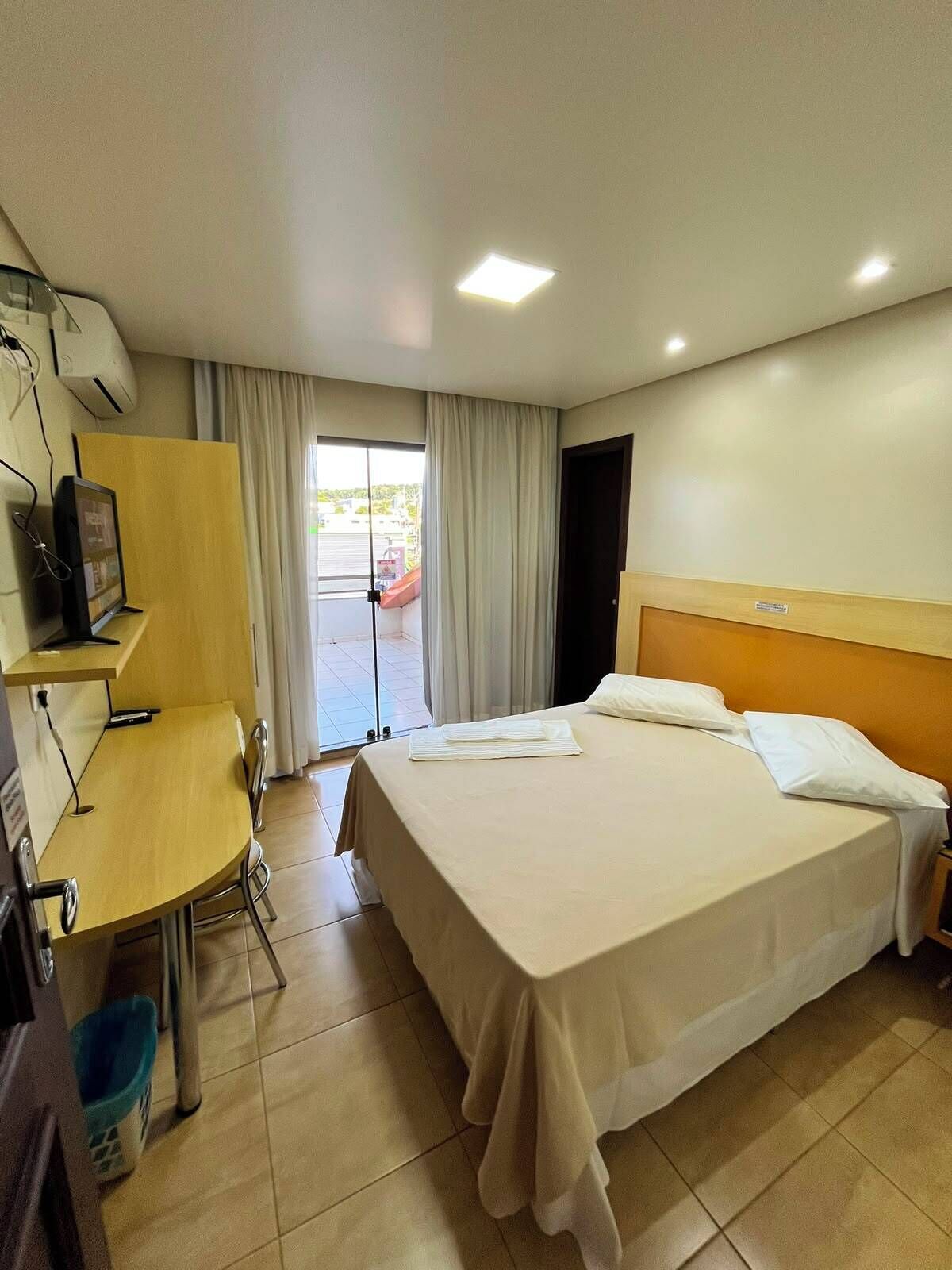Une chambre d’hôtel avec un lit, un bureau, une chaise, une télévision et une fenêtre avec des rideaux.