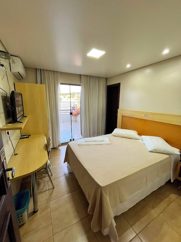 A hotel room with a bed, a desk, a chair, a television, and a window with curtains.