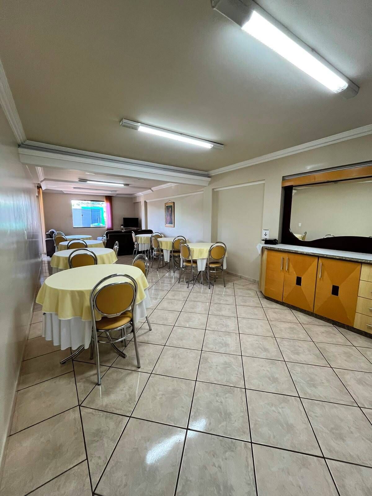 A dining area with tables and chairs, a kitchen area with cabinets, and a television screen in the background.