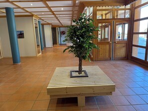 Un hall con un banco de madera, una planta en maceta y piso de baldosas.