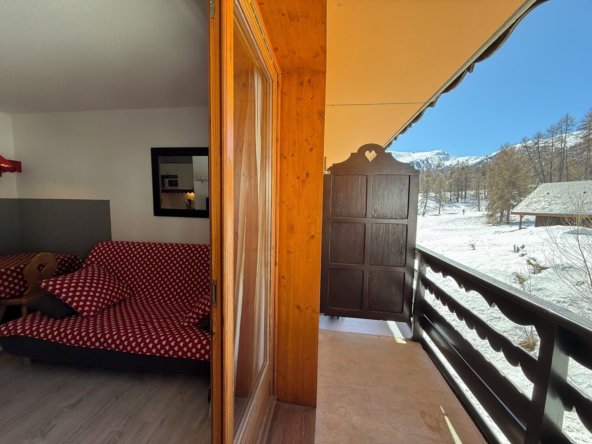 Et værelse med en seng, en trædør og en balkon med udsigt over sneklædte bjerge.