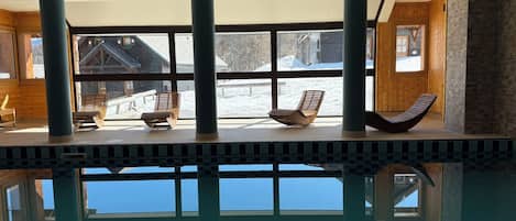 An indoor swimming pool with clear views of a snowy landscape through large windows.