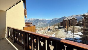 Un balcon avec une balustrade en bois, une vue sur des montagnes enneigées et des bâtiments en arrière-plan.