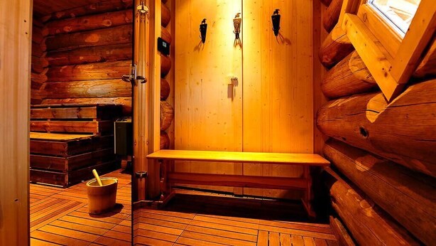 Un sauna en bois, avec des bancs et un seau, des murs en bois et une fenêtre.