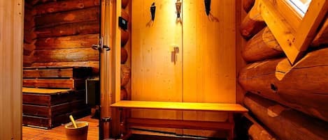 A wooden sauna with benches and a bucket, wooden walls, and a window.