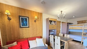 Une pièce chaleureuse avec un mur en bois, un canapé agrémenté de coussins rouges et blancs, une table à manger avec des chaises et un lustre.