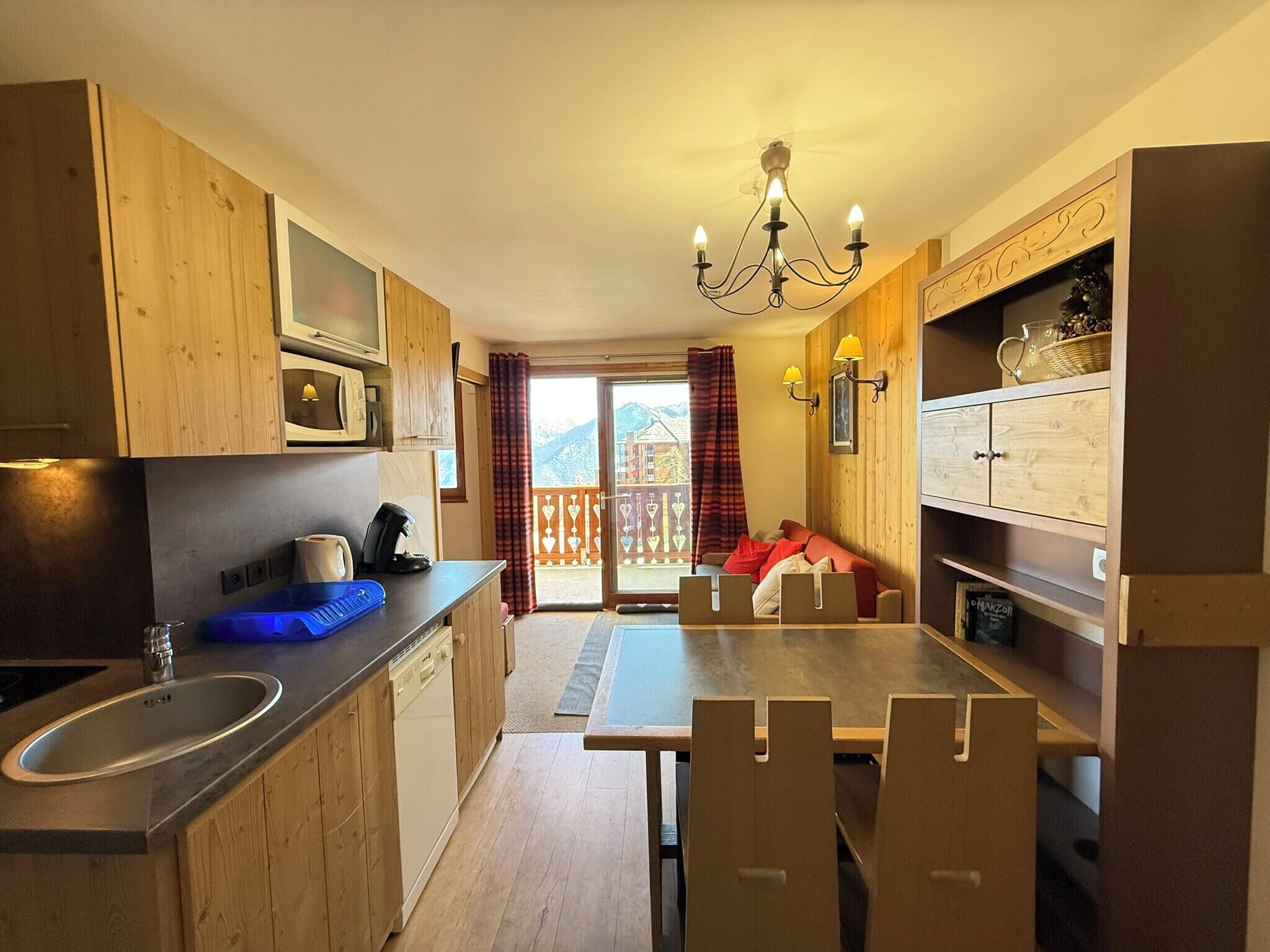 A kitchen with wooden cabinets, a dining table with chairs, a sink, and a view of a balcony with a railing.