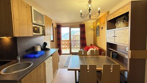 Une cuisine avec des meubles en bois, une table à manger avec des chaises, un évier et une vue sur un balcon doté d’une balustrade.